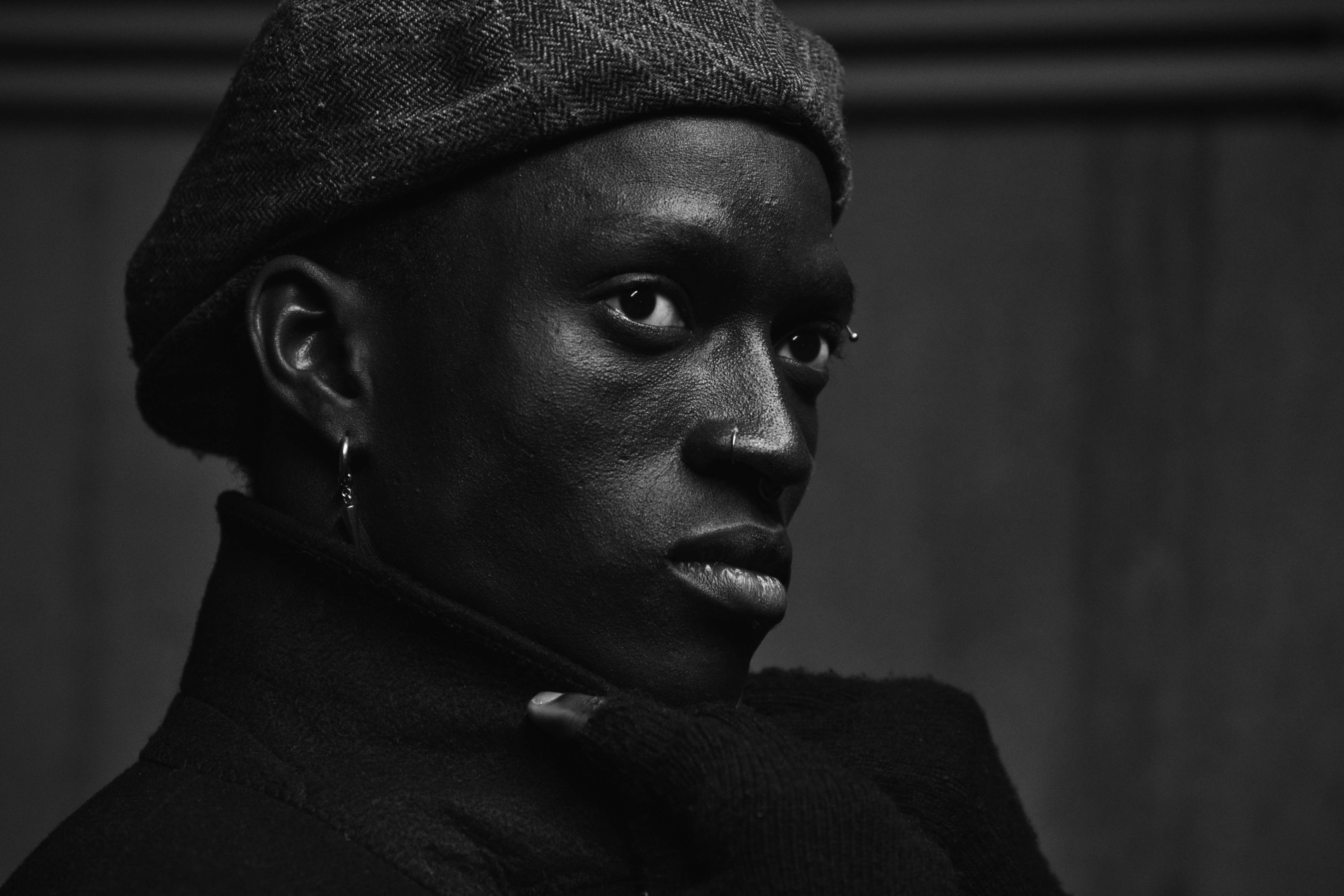 ausdrucksstarkes Schwarz-Weiß-Porträt eines dunkelhäutigen Mannes mit Haube und Mantel, Kelvin Addai