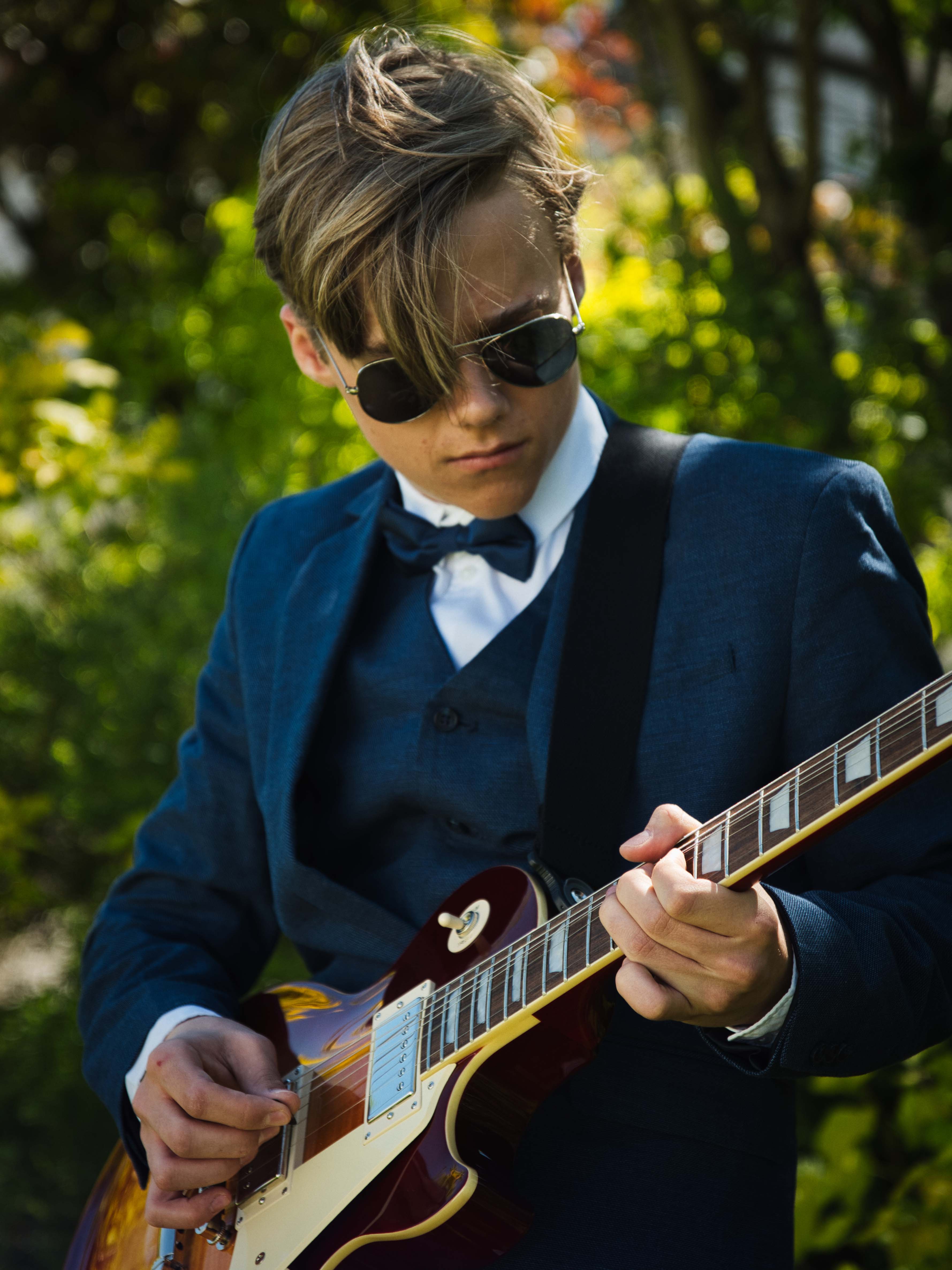 Tobias Lorenz im Anzug und Sonnenbrille spielt konzentriert E-Gitarre, Nahaufnahme in der Natur