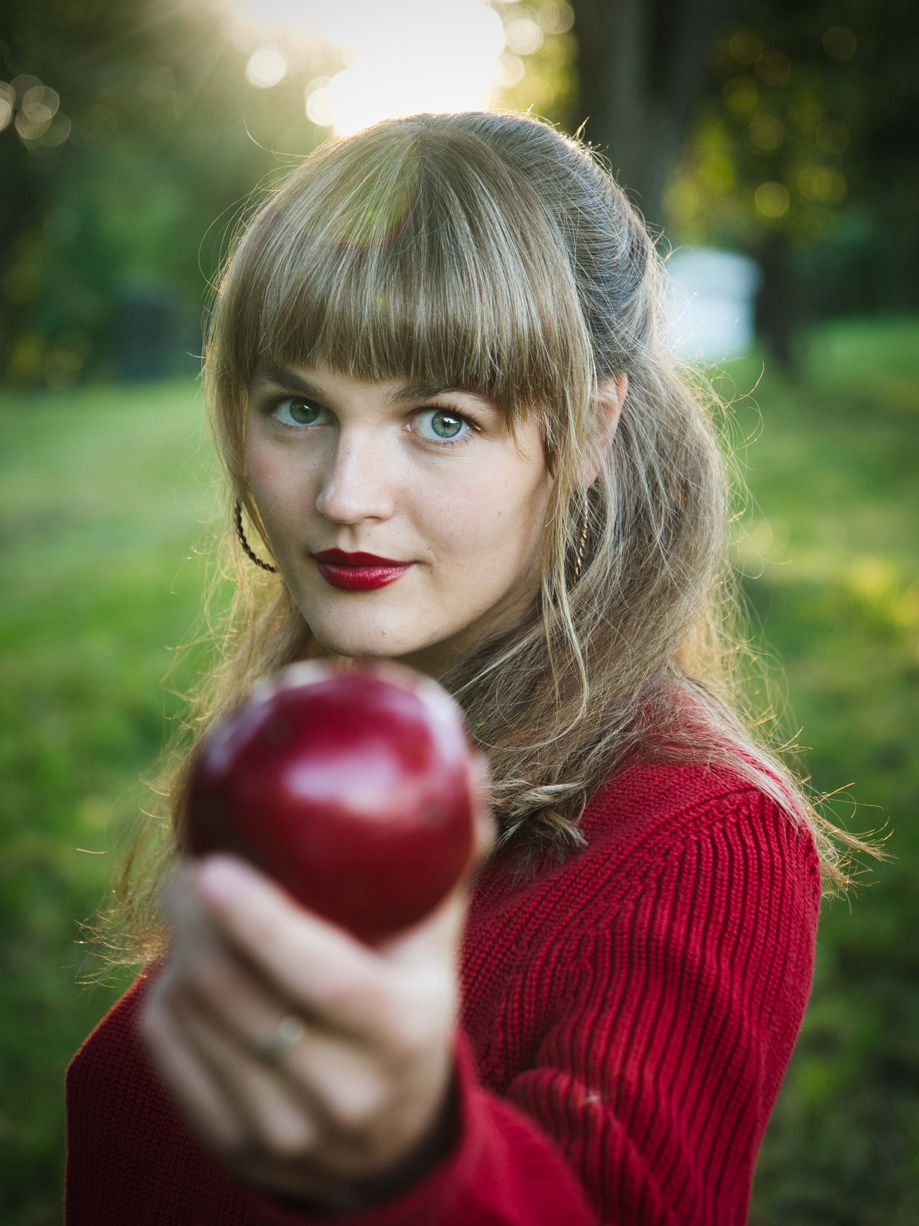 Laura Schmolmüller trägt einen roten Pullover und roten Lippenstift, hält einen roten Apfel, Herbstliches Porträt