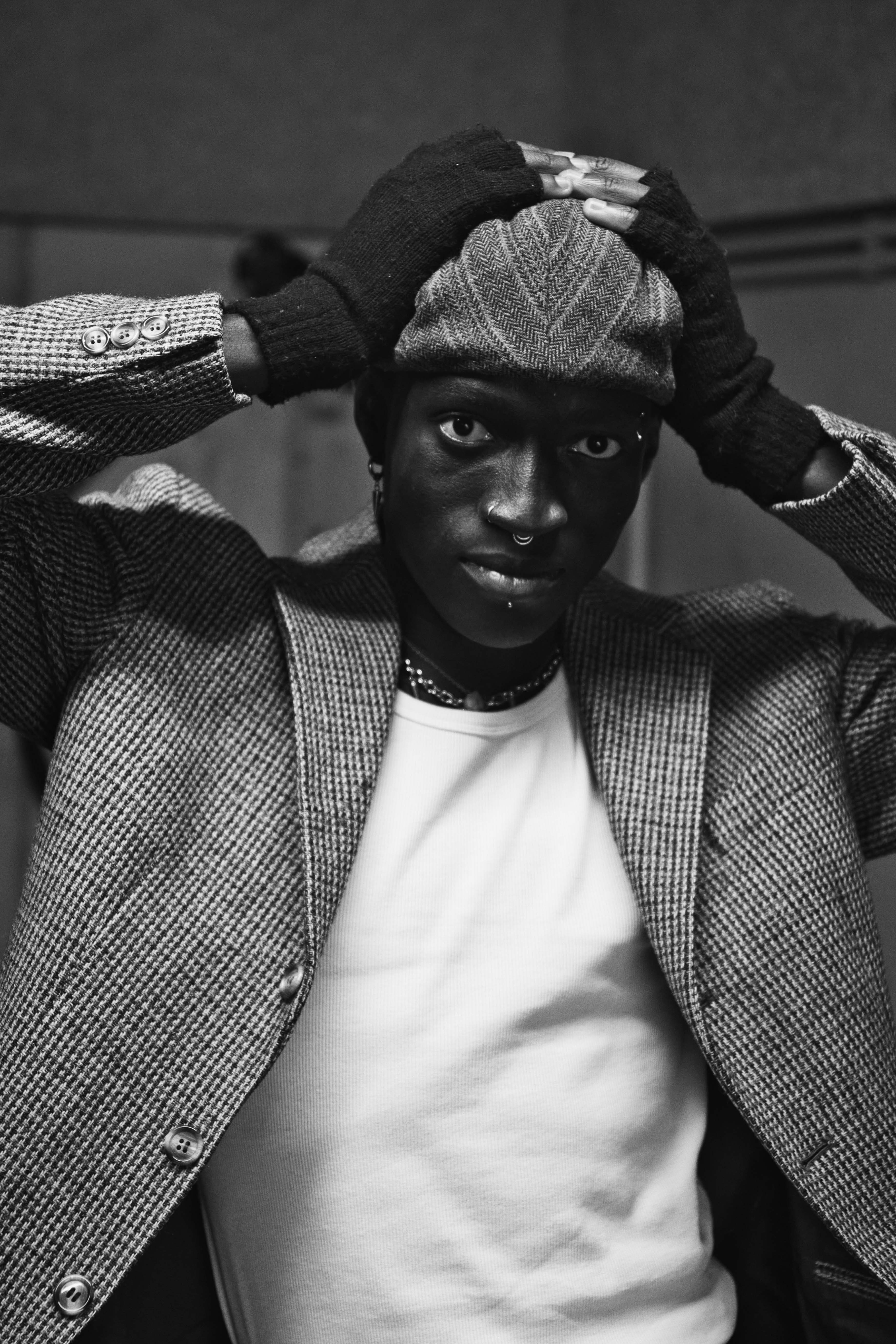 ausdrucksstarkes Schwarz-Weiß-Porträt von Kelvin Addai mit Barett und Handschuhen, fotografiert im Vintage-Stil