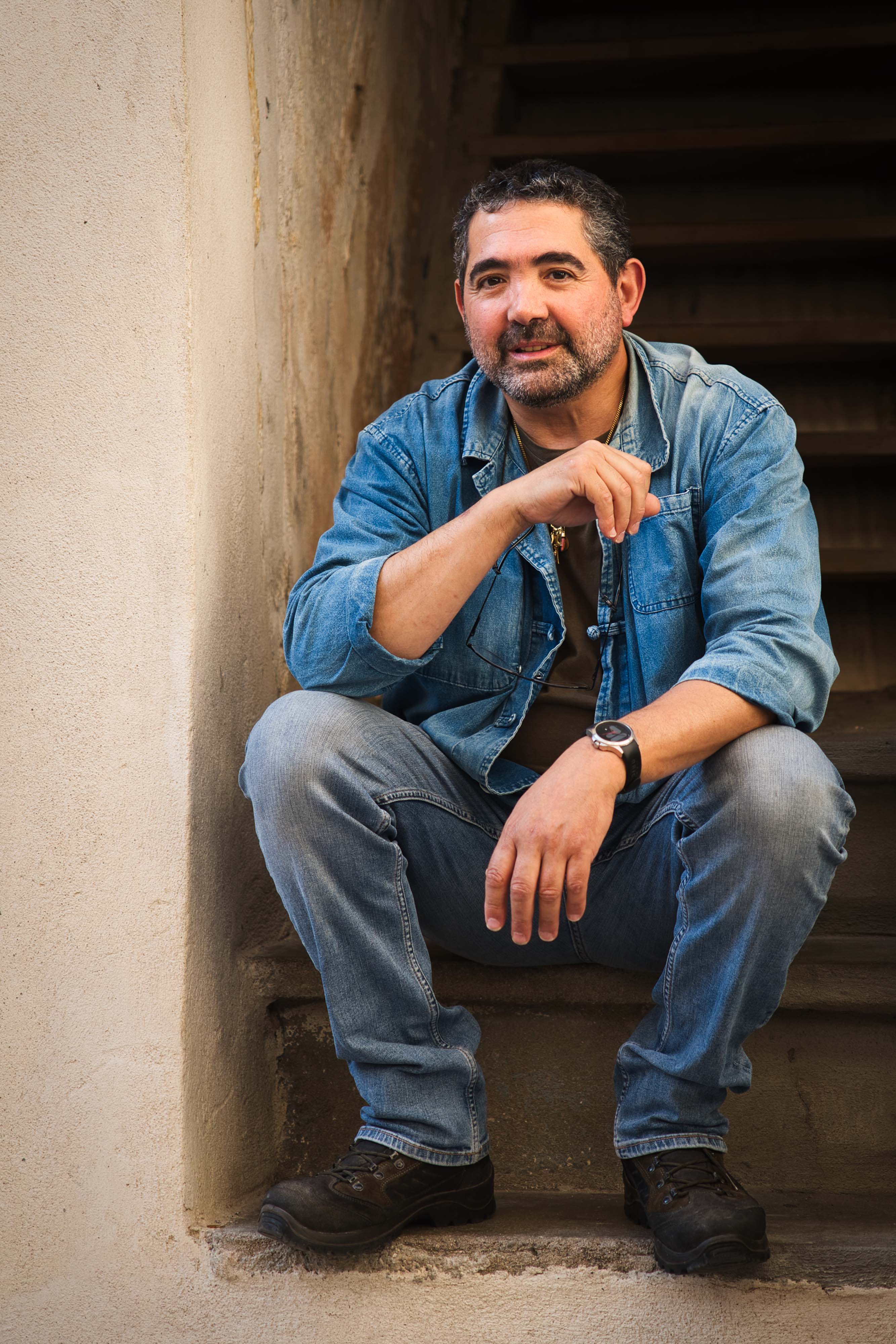 lokaler Mann aus Bonifacio auf Korsika sitzt in Jeansjacke auf einer Steintreppe und blickt freundlich in die Kamera