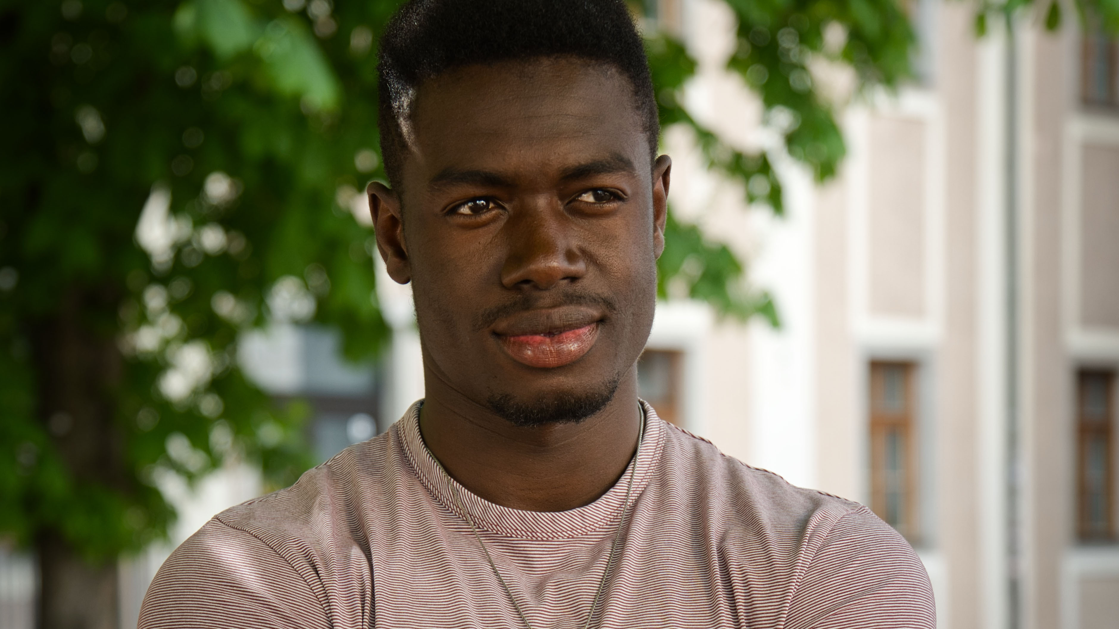 Morr Ndiaye blickt lächelnd in die Ferne, Porträtaufnahme im Freien mit grünen Bäumen im Hintergrund, Crossing Europe Linz