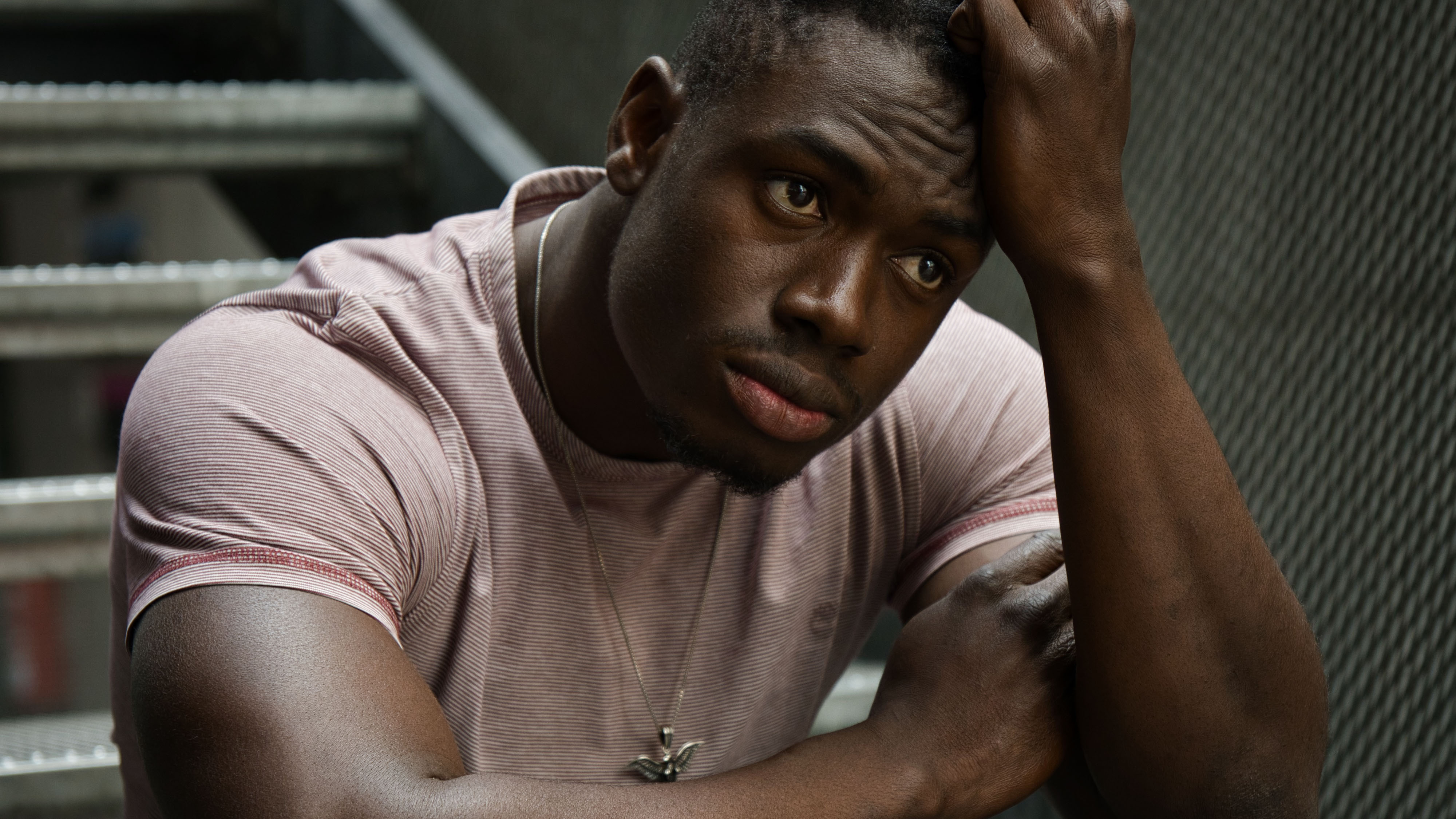 emotionales Porträt eines dunkelhäutigen Mannes auf einer Treppe, nachdenklicher Ausdruck, natürliche Lichtstimmung