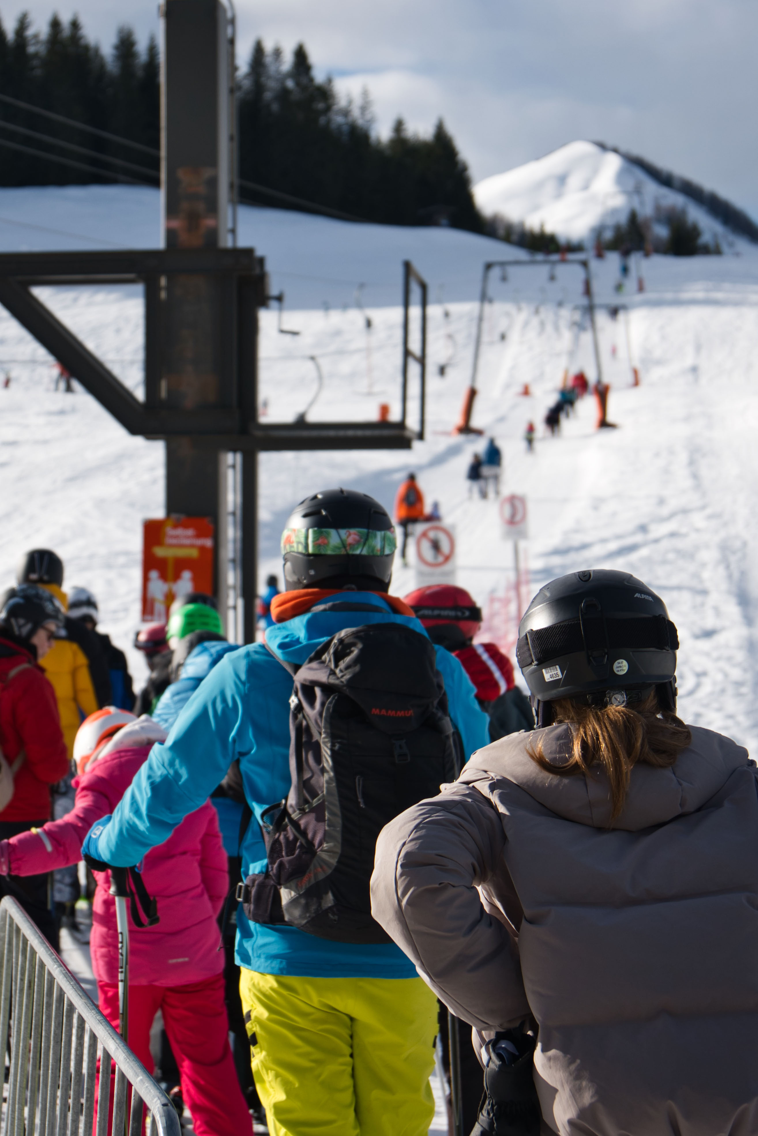 Skifahrer in bunter Winterkleidung warten in der Schlange am Skilift im Postalm Winterpark, verschneite Piste und Berg im Hintergrund