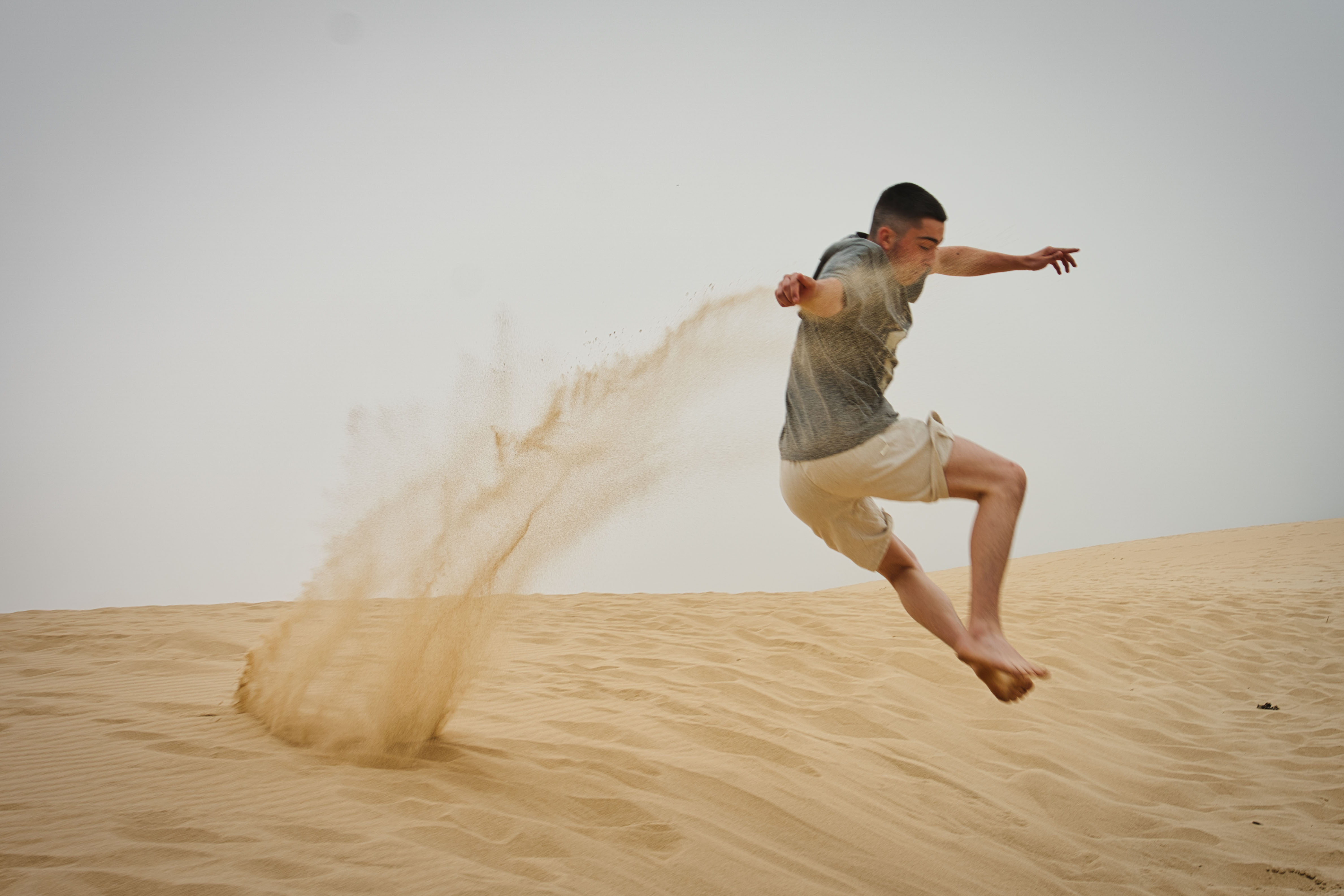 Lorenz Dietrich springt an einem Strand in Portugal, Sand fliegt durch die Luft