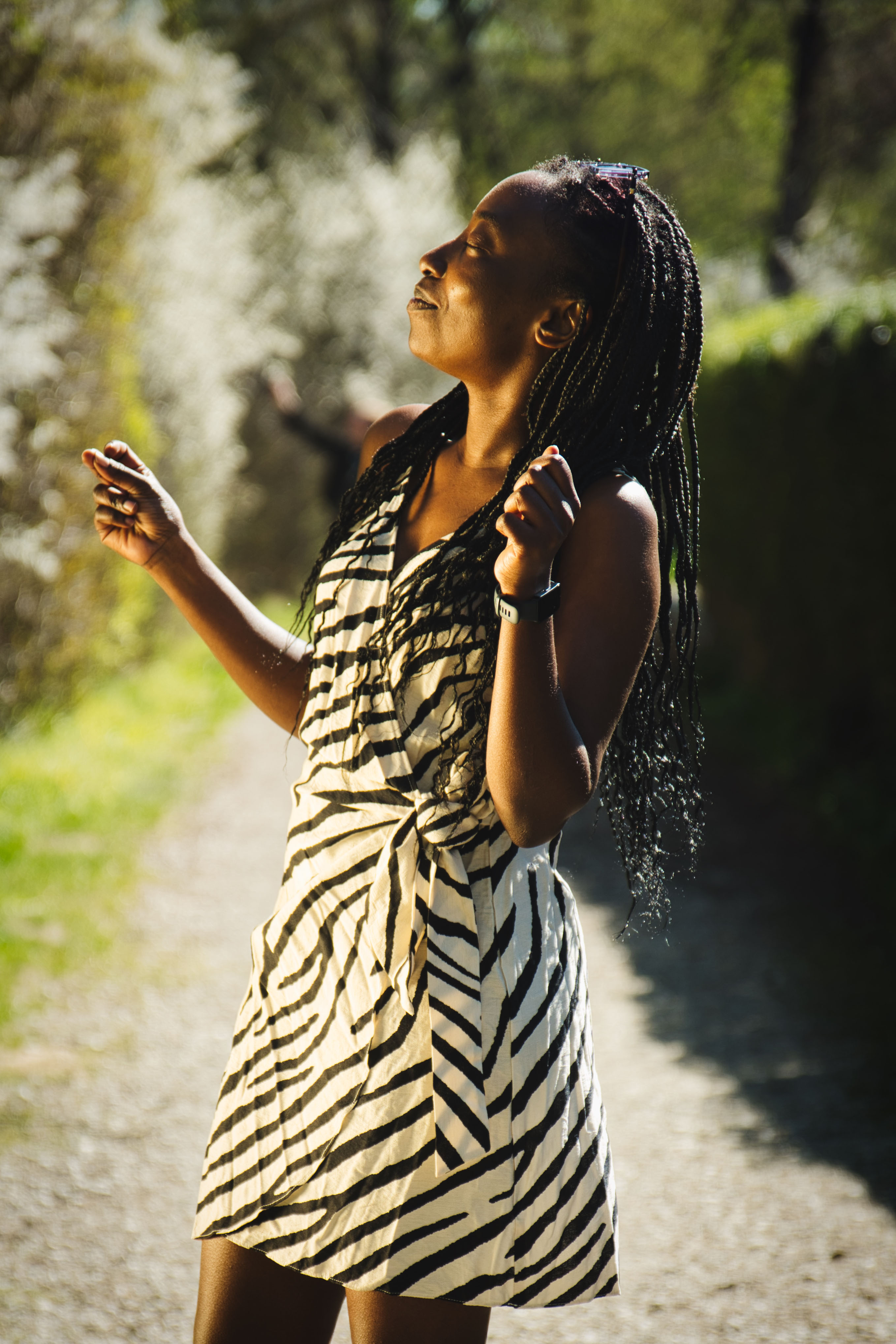 junge, dunkelhäutige Frau in weiß-schwarz gemustertem Sommerkleid tanzt in der Natur