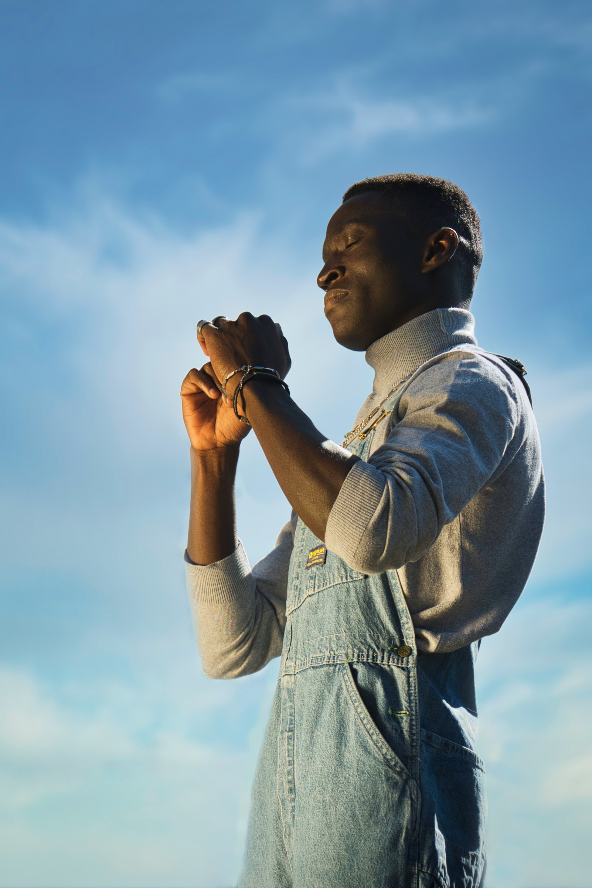 junger, dunkelhäutiger Mann tanzt und trägt eine Latzhose aus Jeansstoff, goldene Stunde
