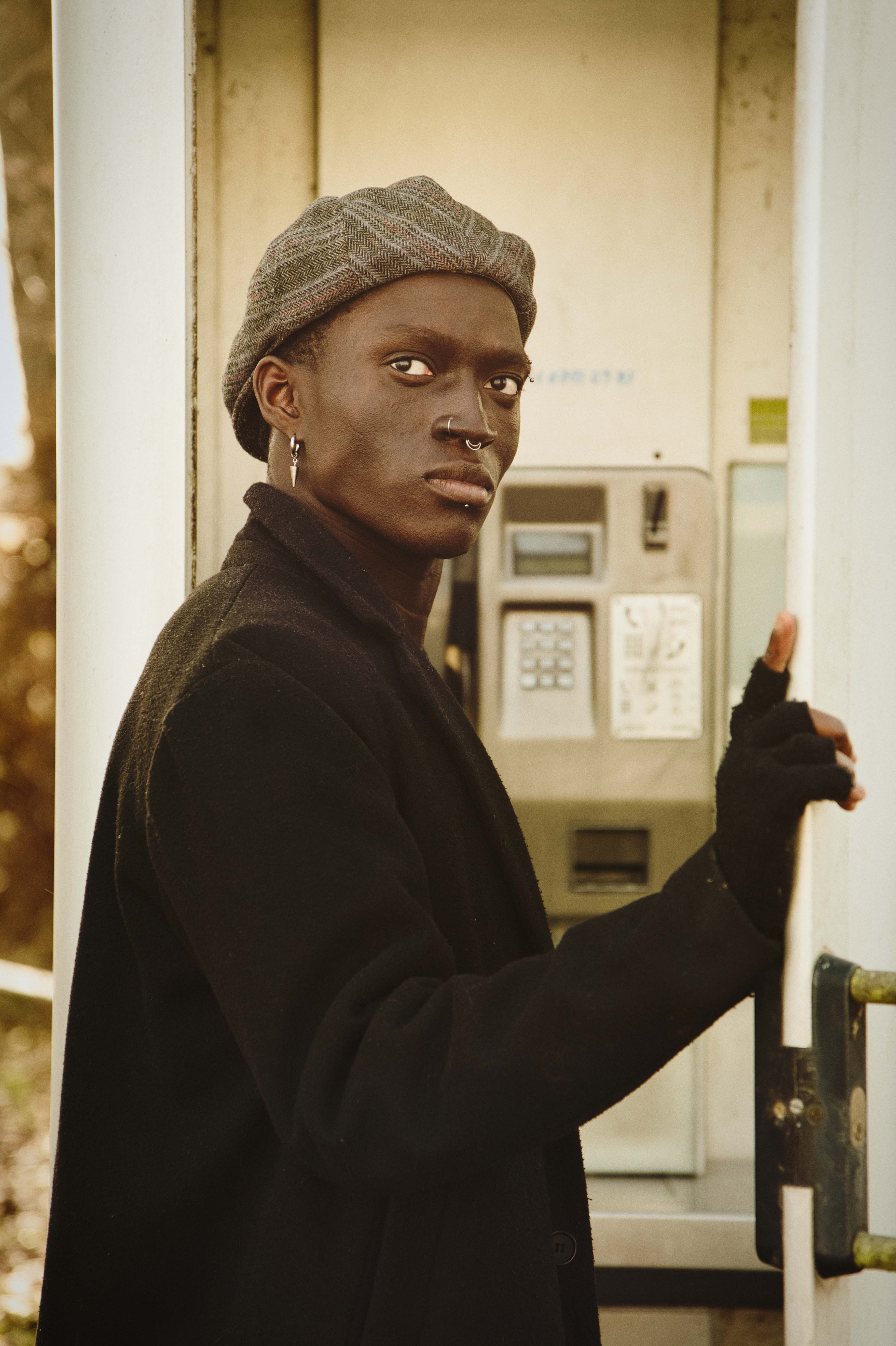 ausdrucksstarkes Porträt von Kelvin Addai vor einer Telefonzelle in Linz, fotografiert im Vintage-Style